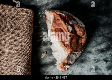 high angle view of a half round kamut wheat bread loaf on a mottled dark gray fabric surface, next to a burlap sack Stock Photo