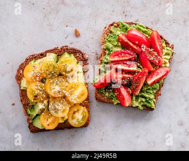 Overhead view of two toasted sourdough slices with avocado and yellow and red tomatoes
