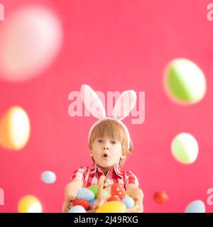 Surprised child holding basket with Easter eggs. Funny kid wearing Easter bunny. Child having fun at home. Spring holidays concept Stock Photo