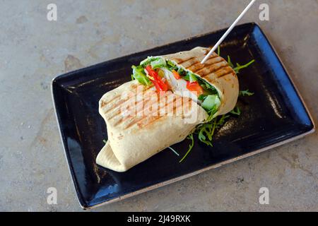Tortilla wrap filled with chicken and vegetables on a black plate and a marble table, Mexican food, copy space, selected focus, narrow depth of field Stock Photo