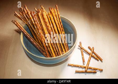 Pretzel sticks in a bowl on a wooden table, crunchy salt snack, typical served in the evening, in pubs, on a party or at home while watching TV, copy Stock Photo