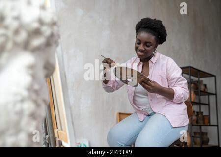 A smiling dark-skinned artist mixing colors on palette Stock Photo