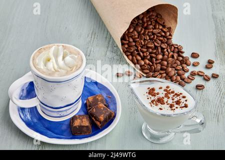 Cup of coffee with whipped cream and milk, chopped chocolate and a bag of coffee beans on a blue wooden table. Vienna coffee Stock Photo