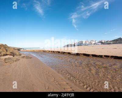 Praia das Maçãs beach of the Sintra coastline, Portugal on a sunny winter day - a beautiful view of the sandy beach and village, large white waves and Stock Photo