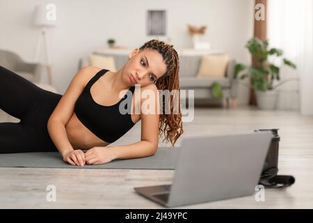 Discontented African Woman Near Laptop Lying Tired Of Exercising Indoor Stock Photo