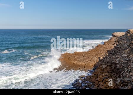 Praia das Maçãs beach of the Sintra coastline, Portugal on a sunny winter day - a beautiful view of the sandy beach and village, large white waves and Stock Photo