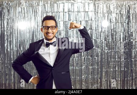 Happy confident young black man in suit smiling and flexing his arm with strong muscles Stock Photo