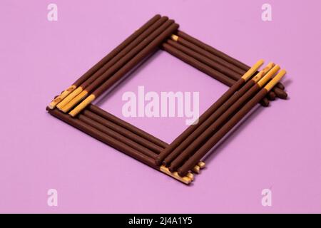 Chocolate covered sticks stacked in a square on purple background Stock Photo