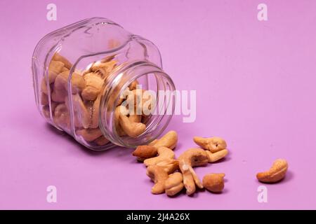 Cashew nuts spilled from a square-shaped glass jar on a purple background Stock Photo
