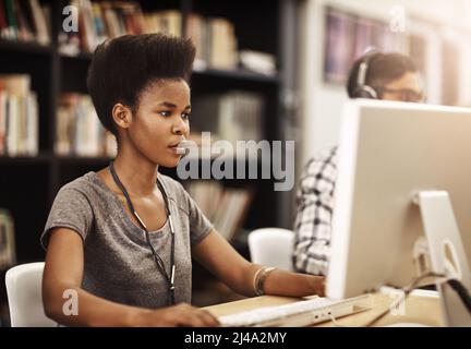 The library has many resources to use. Shot of university students working on computers in the library on campus. Stock Photo