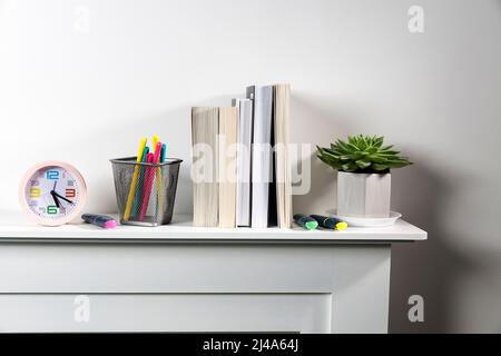 Echeveria in geometric pot, stack of books, pens in a pencil holder, felt-tip pens, are on shelf. Place for text Stock Photo