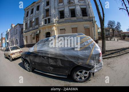 View of a car without windows wrapped in film and residential building with broken windows. Russian army bombed civilian objects. Rocket bomb attack. Stock Photo