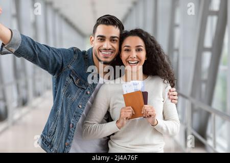 Happy Travellers. Jouful Young Arab Couple Taking Selfie At Airport, Holding Passports Stock Photo