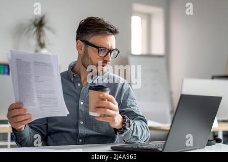 Mature man CEO of IT company sitting at workplace in front of laptop, reading report and looking at computer screen Stock Photo