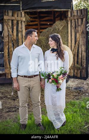 Beautiful wedding couple. The groom hugs the bride tightly and kisses. The bride holds a bouquet and laughs. Rustic wedding in the style of boho at th Stock Photo