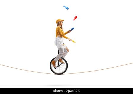 Young female riding a unicycle on a tightrope and juggling isolated on white background Stock Photo