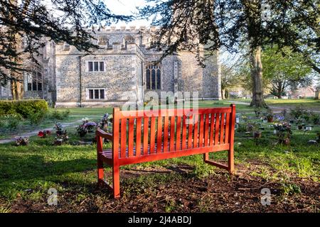 A red bench catching the last of the sunset, a striking place of contemplation and memorial. In the churchyard of St. Peter ad Vincula in Coggeshall, Stock Photo