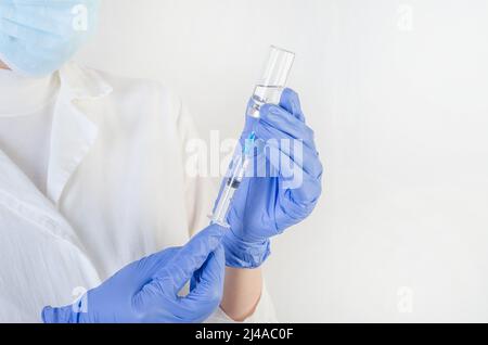 Female doctor in a protective blue suit with a syringe on a white background with copy space. Stock Photo