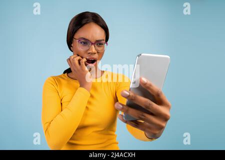 Shocked millennial african american woman in glasses with open mouth reads message on phone Stock Photo