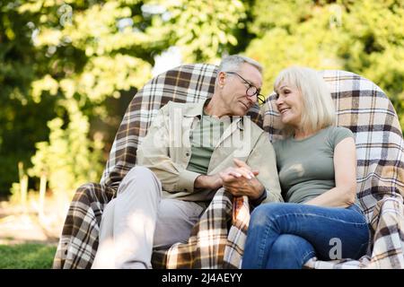 Loving senior married couple resting in their garden in countryside, sitting in wicker chairs and looking at each other Stock Photo