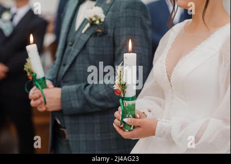 The bride and groom hold shining candles during the ceremony in the church. Hands of newlyweds with candles in the church. Church religious details Stock Photo