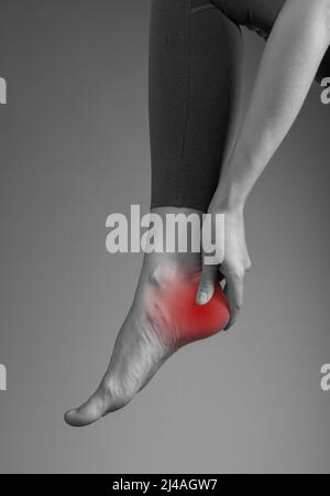 Pain in foot heel. Woman holding leg with red point closeup. Neurologic, rheumatologic, traumatic causes. Health care and medicine concept. High quality photo Stock Photo