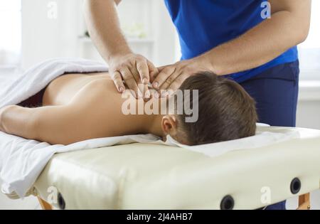 Young man lying on massage table and enjoying professional therapeutic neck massage Stock Photo
