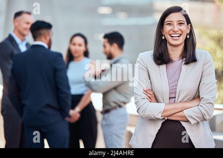 Ive got a team that can make it happen. Shot of an attractive young businesswoman standing outside with her arms folded while her colleagues stand Stock Photo