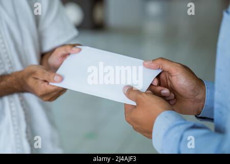 hand giving envelope as a charity donation at the mosque during ramadan Stock Photo