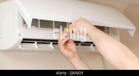 The master unscrews the air conditioner cover with a screwdriver. Professional maintenance and repair of air conditioners Stock Photo
