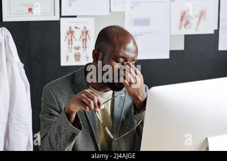 African man rubbing his eyes tired of his work on computer while working at office Stock Photo