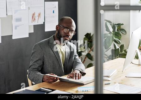 African businessman in eyeglasses reading a book while sitting at workplace at office Stock Photo