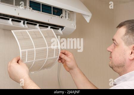 The master removes the dusty filter of the air conditioner. Maintenance and repair of air conditioners. Stock Photo