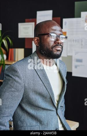African serious businessman in eyeglasses looking thoughtful while standing at office Stock Photo