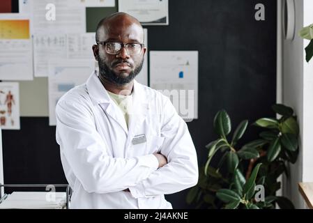 Portrait of confident African practitioner standing in lacoat with his arms crossed and looking at camera with serious expression Stock Photo