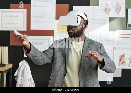 African businessman standing in goggles and gesturing during virtual reality game Stock Photo