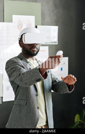 Black young man using virtual reality goggles while working at office Stock Photo