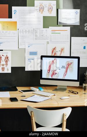 Image of computer with medical presentation on monitor for online education with medicine poster on wall in background Stock Photo