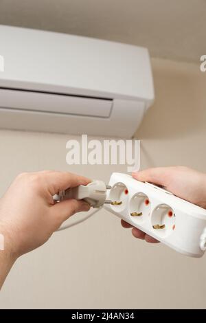The person plugs the air conditioner plug into the outlet Stock Photo