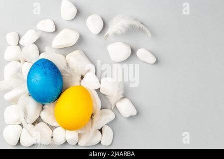 Blue and Yellow Ukrainian Easter Eggs on the rocks scattered on the grey background. National flag colors. Support Ukraine Stock Photo