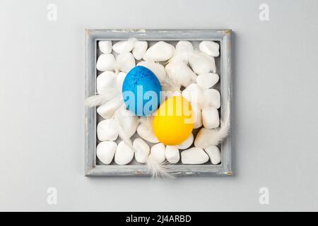 Easter Eggs on the rocks surrounded by the gray frame. Ukrainian Blue and Yellow National flag colors. Support Ukraine Stock Photo