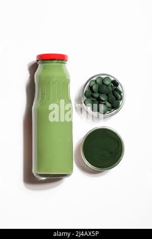 green smoothie in bottle and spirulina algae powder and pills in glass bowl on white background.useful habits,self care and healthy lifestyle concept. Stock Photo