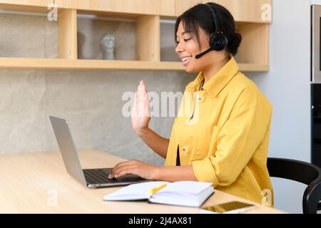 Young thoughtful African American female sudent in a headset is listening to an online webinar, studing remotely from home or working in the customer service department as a call center operator Stock Photo