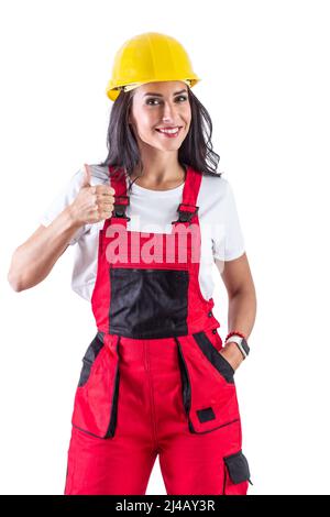 Glamorous brunette wearing contruction workers clothes and yellow helmet. Also doing a thumb up sign. Isolated background. Stock Photo