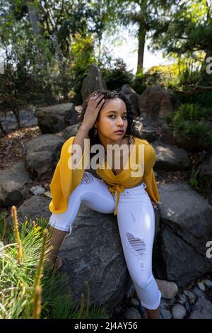 Beautiful Young Black Woman Seated on Rocks in a Japanese Garden Stock Photo