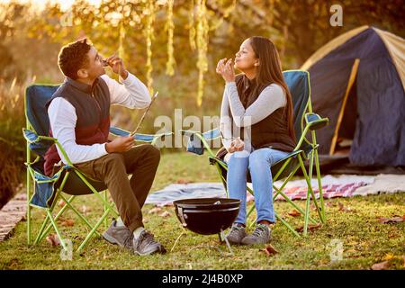 Its all good in the woods. Shot of a young couple roasting marshmallows while camping outside. Stock Photo