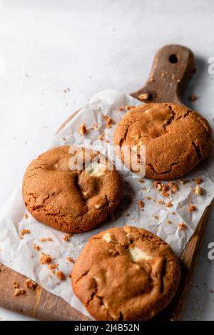 Three gingerbread and white chocolate cookies on a wooden chopping board. Stock Photo