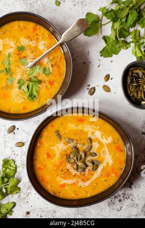 Bowls of carrot soup with fresh coriander, pumpkin seeds and coconut milk garnishes. Stock Photo