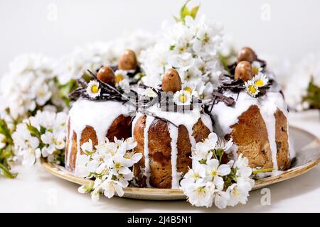 Homemade traditionla Easter cake with chocolate nests and eggs on ceramic plate and blossoming cherry tree over white background. Traditional ortodox Stock Photo