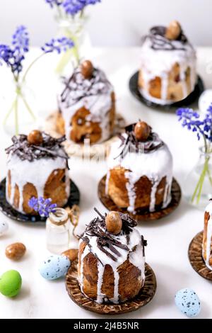 Homemade traditionla small Easter kulich cakes with chocolate nests and eggs on plates decorated with muscari flowers over white background. Tradition Stock Photo